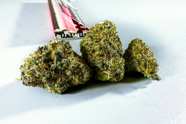 Close-up of three dense cannabis buds resting on a surface, with a branded packaging in the background