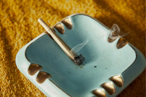 A lit cannabis joint resting in a light blue ashtray with golden accents