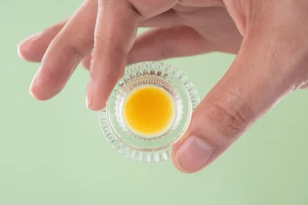 Hand holding a small glass container of cannabis concentrate, showcasing a bright yellow texture