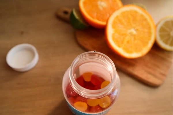 Open jar of cannabis gummies next to fresh orange and lemon slices on a wooden cutting board 