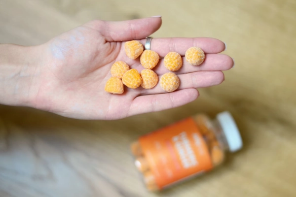 Hand holding bright orange cannabis gummies over a blurred background with a gummy jar visible