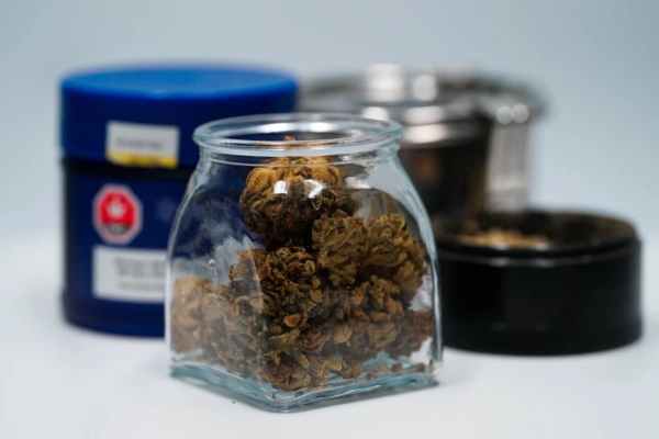 Glass jar filled with cannabis buds next to cannabis storage containers