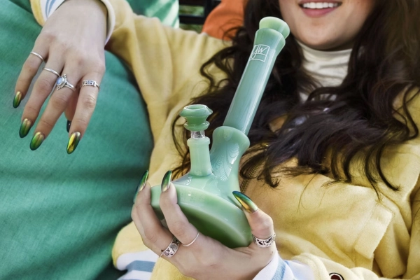 A person holding a pastel green bong while lounging in a cozy setting